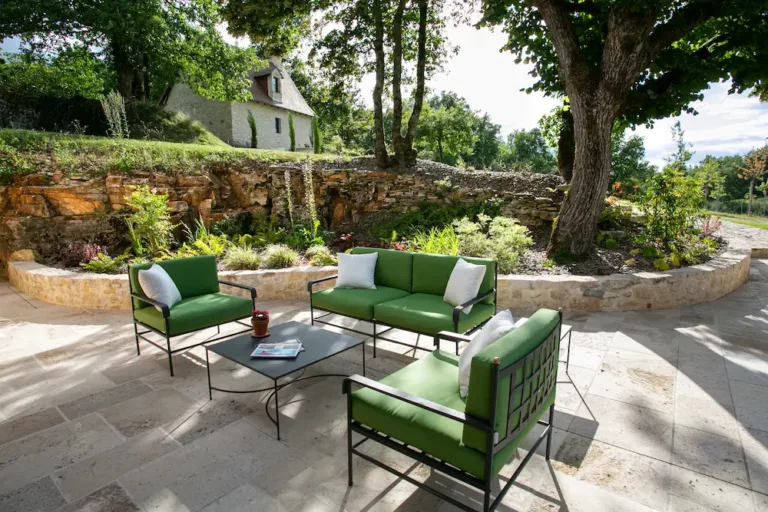 Coin détente sur une terrasse extérieure dallée, habillée d'une composition d'arbres et de fleurs avec un effet surélevée grâce a de la pierre.